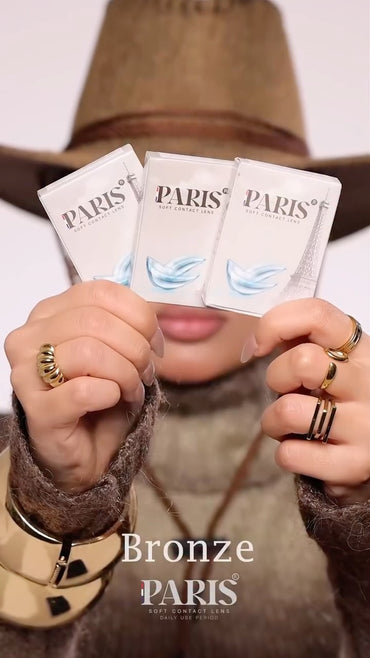 Three 'Bronze Paris' product packets held by a person wearing rings.