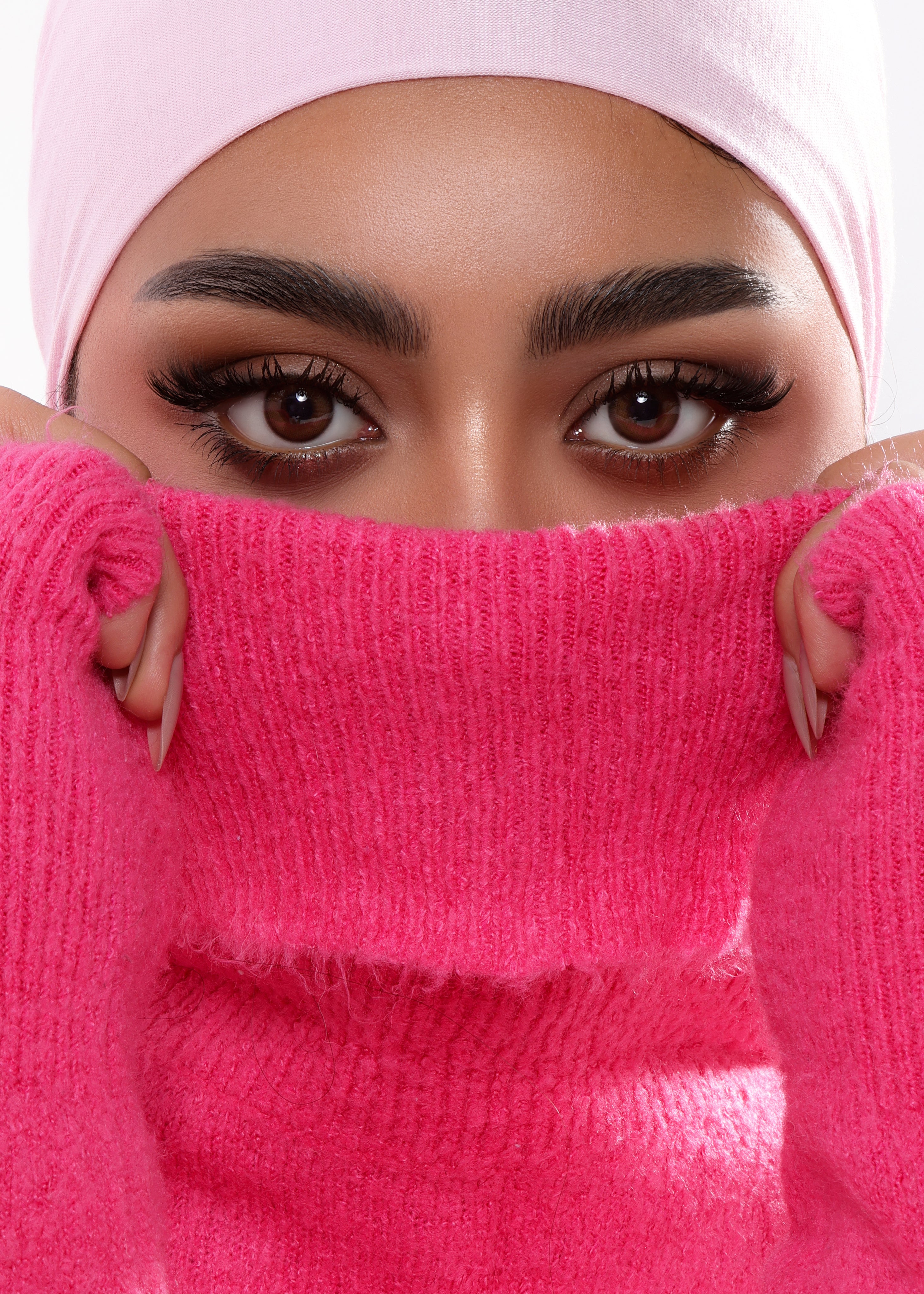 Person wearing a pink headscarf and pink sweater, covering their face.